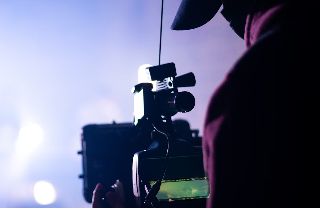 FX Productions Canada A person operating a professional video camera is shown in silhouette against a blurred, brightly lit background, capturing the essence of cinematic storytelling offered by expert video production services. Toronto Video Production Company