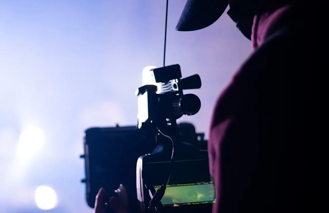 FX Productions Canada A person operating a professional video camera is shown in silhouette against a blurred, brightly lit background, capturing the essence of cinematic storytelling offered by expert video production services. Toronto Video Production Company