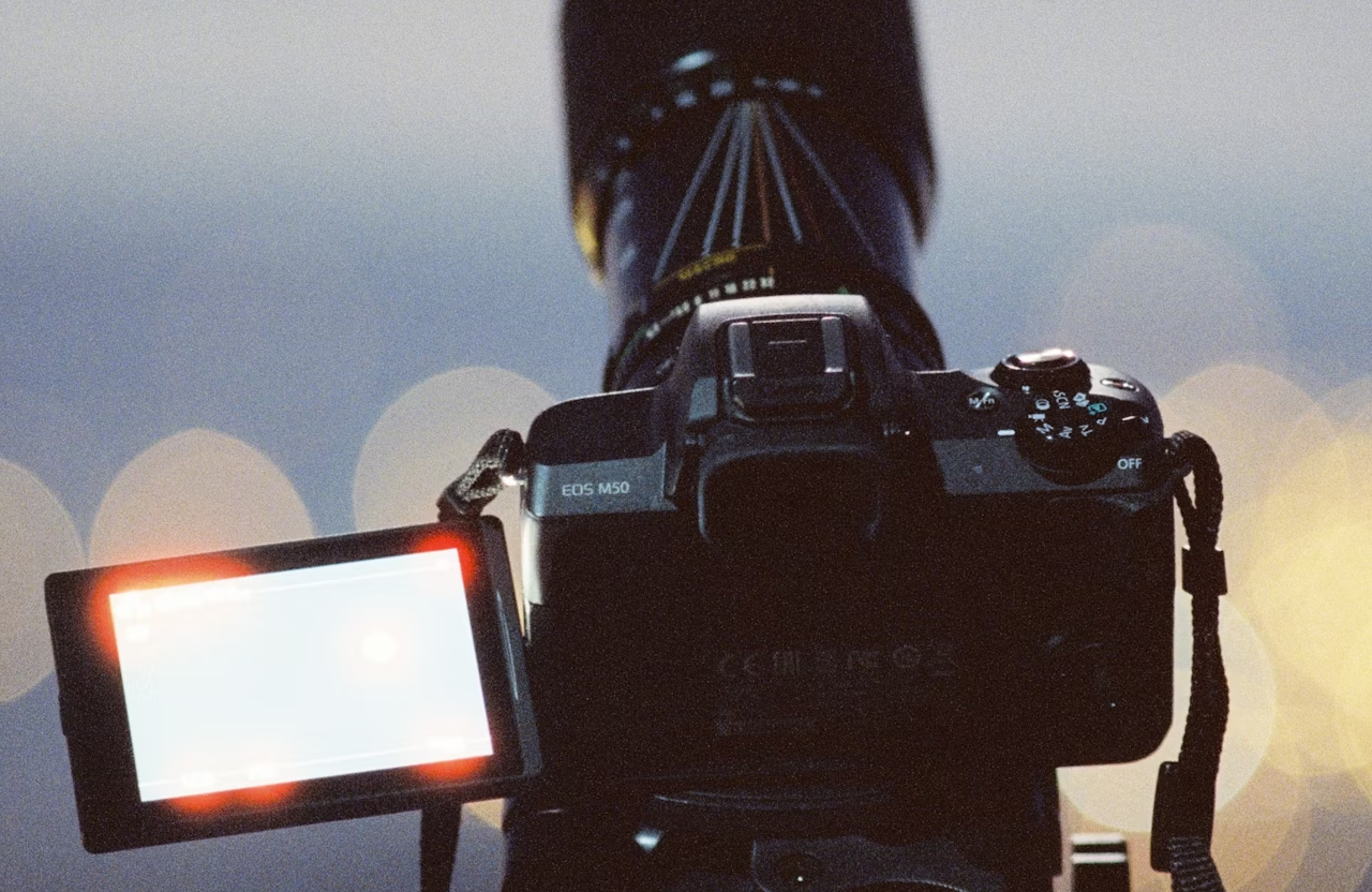 FX Productions Canada A digital camera with a large lens and an open flip-out screen is set up on a tripod, ready for cinematic storytelling—perfect for those seeking professional video production services. Blurred lights glow softly in the background. Toronto Video Production Company