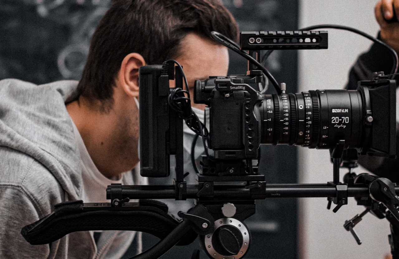 FX Productions Canada A person in a gray hoodie is positioned behind a professional video camera setup with various attachments indoors, capturing cinematic storytelling for full service video production. Toronto Video Production Company