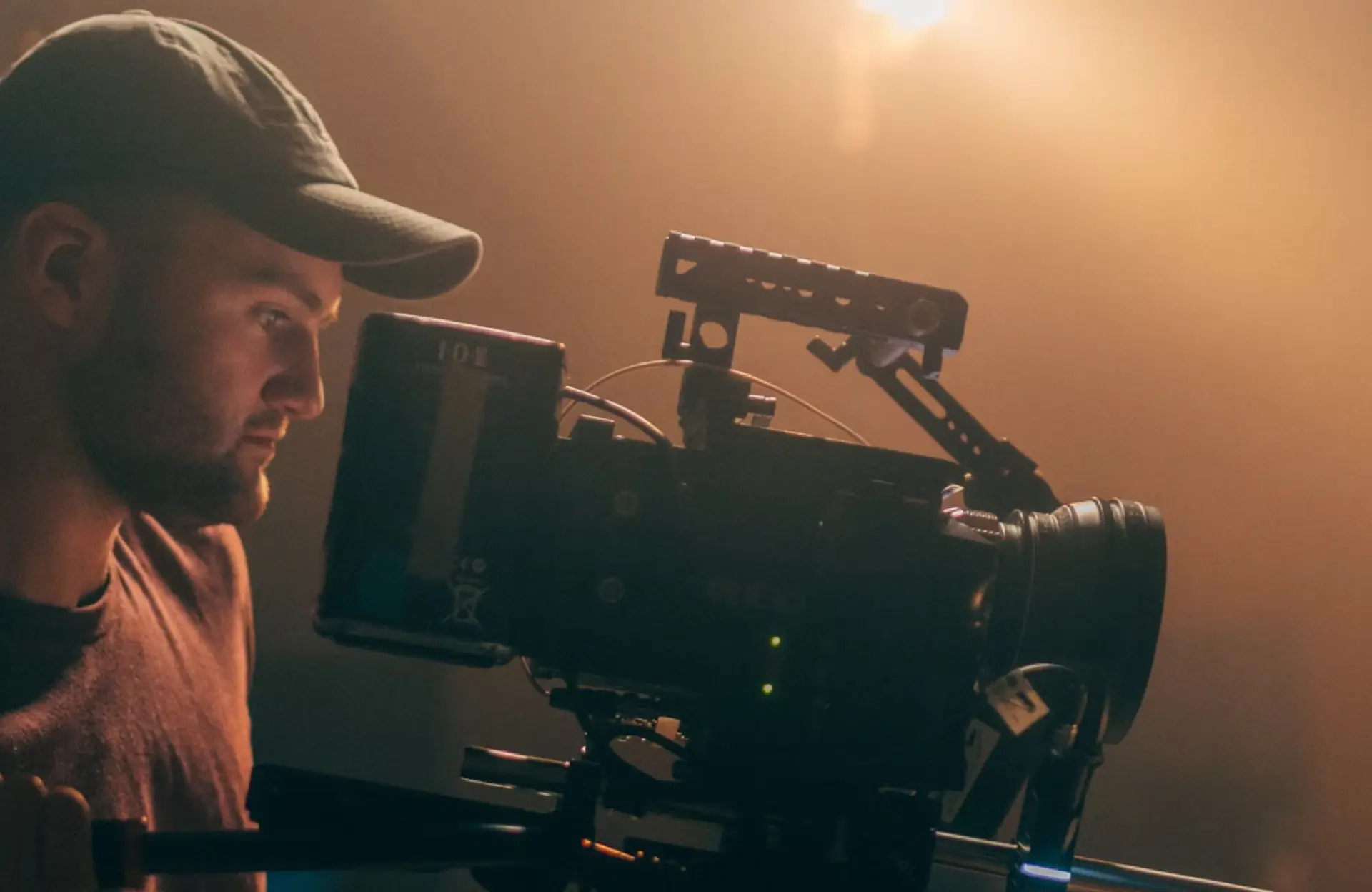 FX Productions Canada A person wearing a cap operates a professional video camera on a film set with warm lighting in the background. Toronto Video Production Company