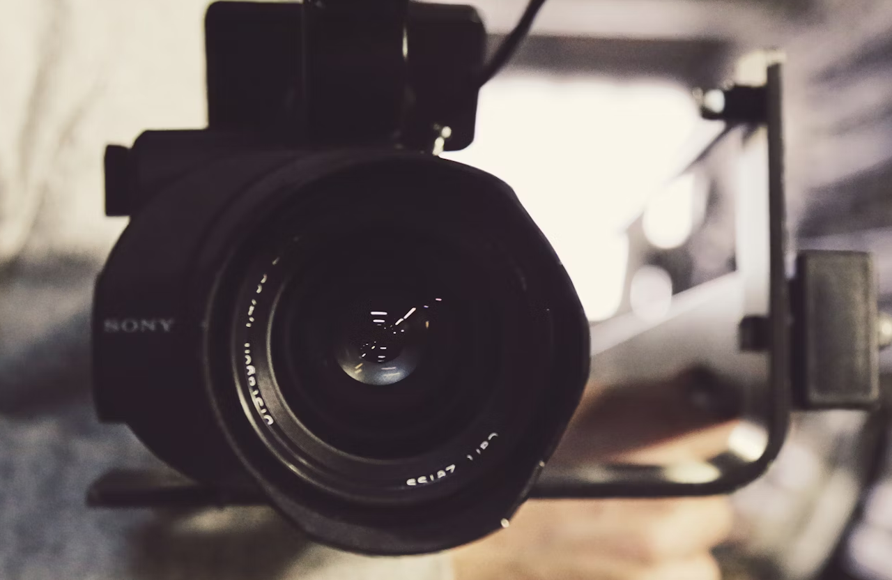 FX Productions Canada Close-up view of a professional Sony video camera lens, with blurred background and a person’s hand holding the camera rig—perfect for a video production company focused on cinematic storytelling to elevate your brand. Toronto Video Production Company