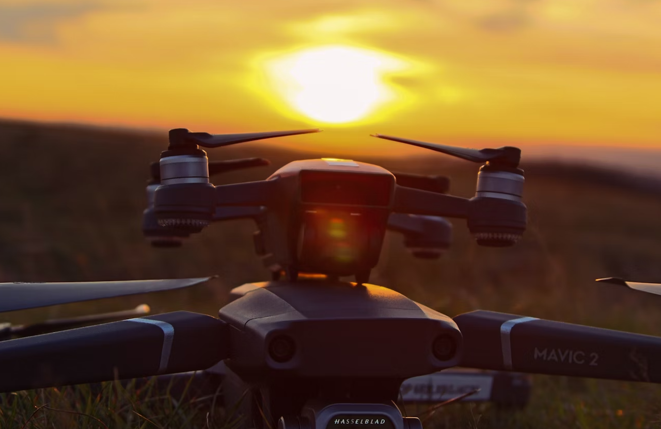 FX Productions Canada Close-up of a DJI Mavic 2 drone on grass at sunset, with the sun low on the horizon casting a warm glow—an ideal scene for capturing stunning drone videography. Toronto Video Production Company
