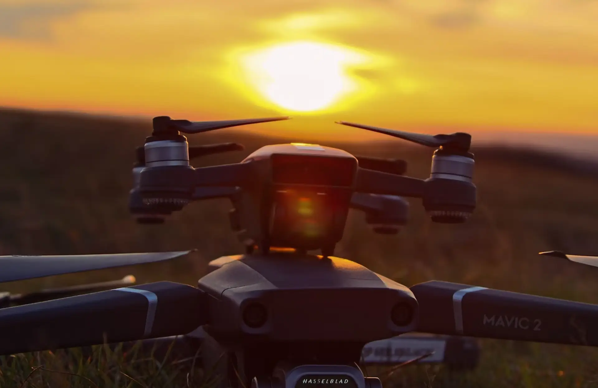 FX Productions Canada Close-up of a DJI Mavic 2 drone on grass at sunset, with the sun low on the horizon casting a warm glow—an ideal scene for capturing stunning drone videography. Toronto Video Production Company
