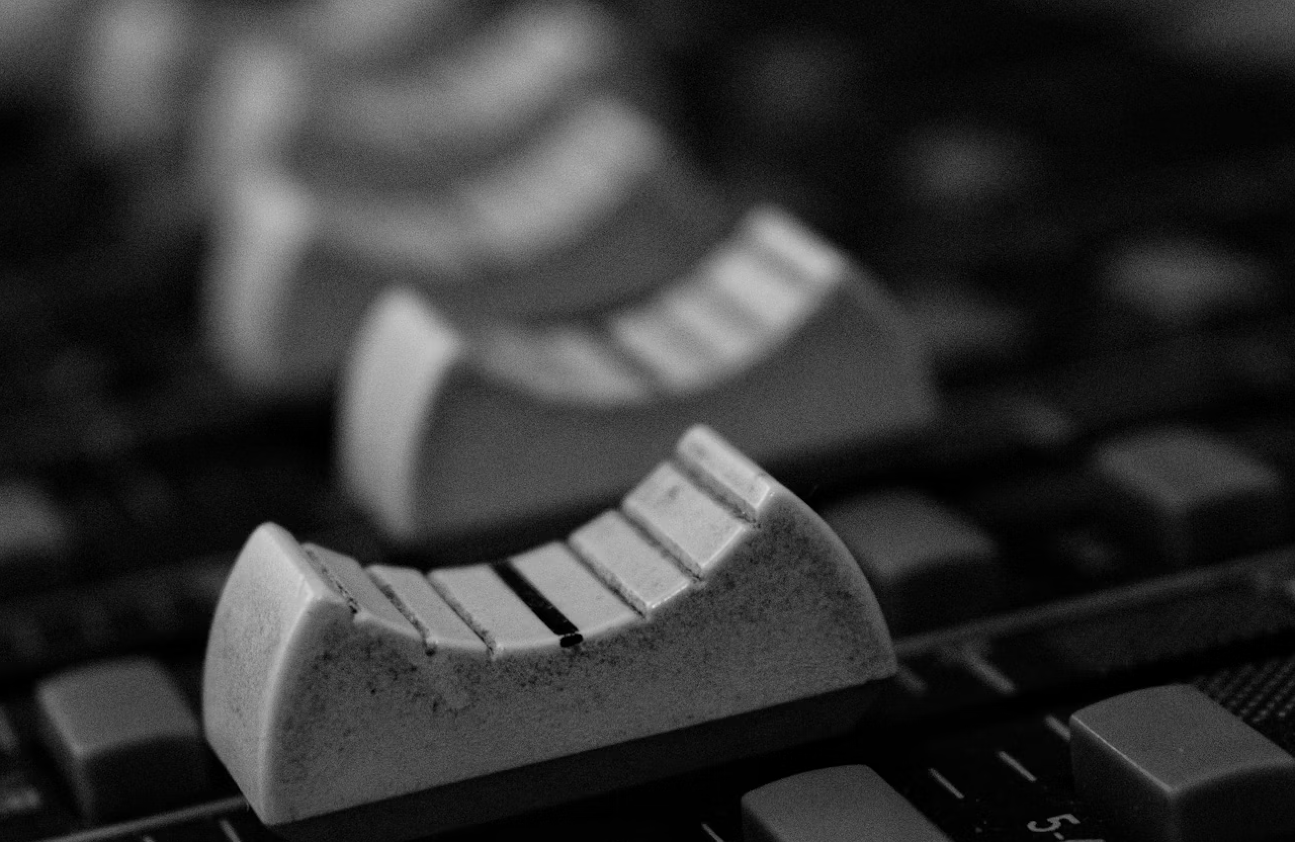 FX Productions Canada Close-up view of audio mixing board faders in black and white, with the focus on one slider in the foreground and others blurred in the background. Toronto Video Production Company
