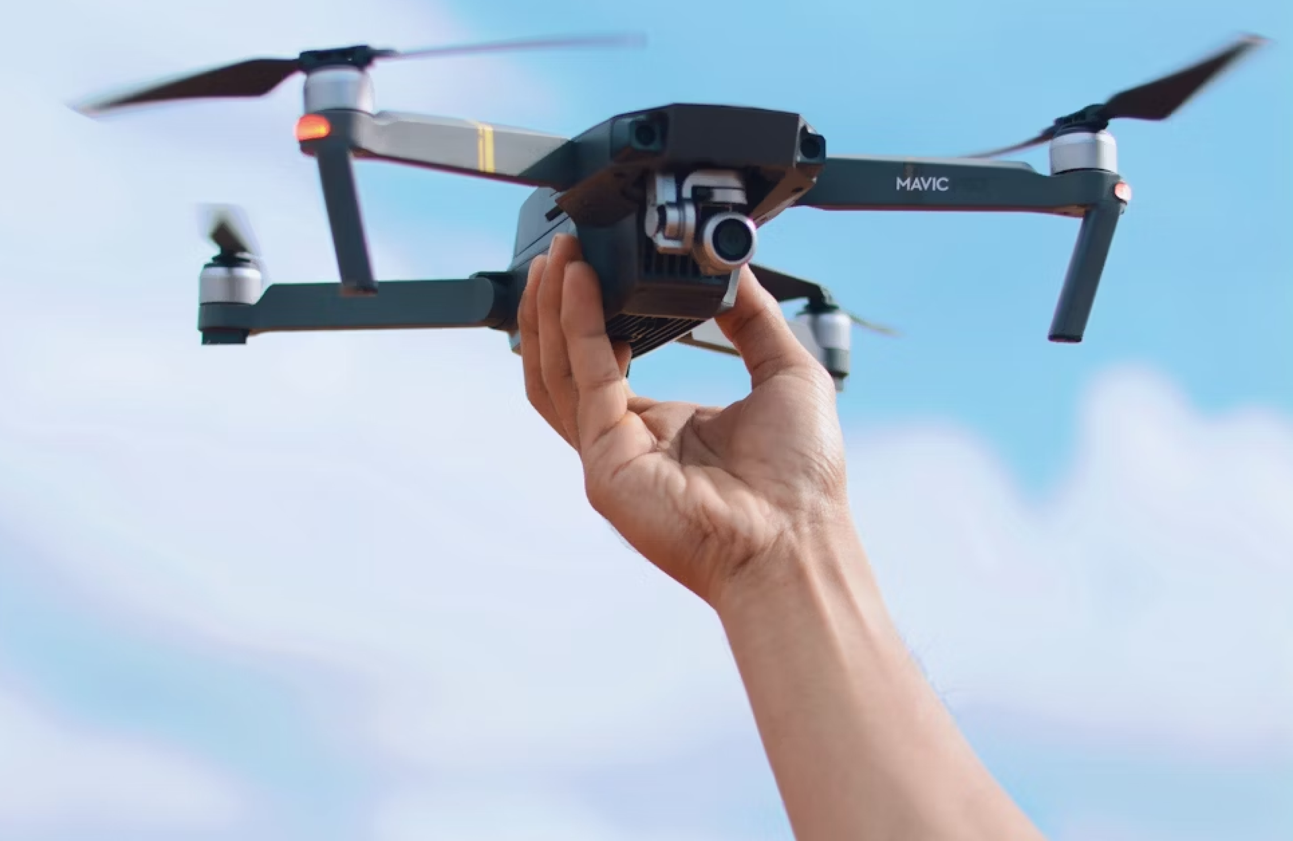 FX Productions Canada A person holds a black quadcopter drone with a camera and the label "Mavic," ready for drone videography, against a clear blue sky. Toronto Video Production Company