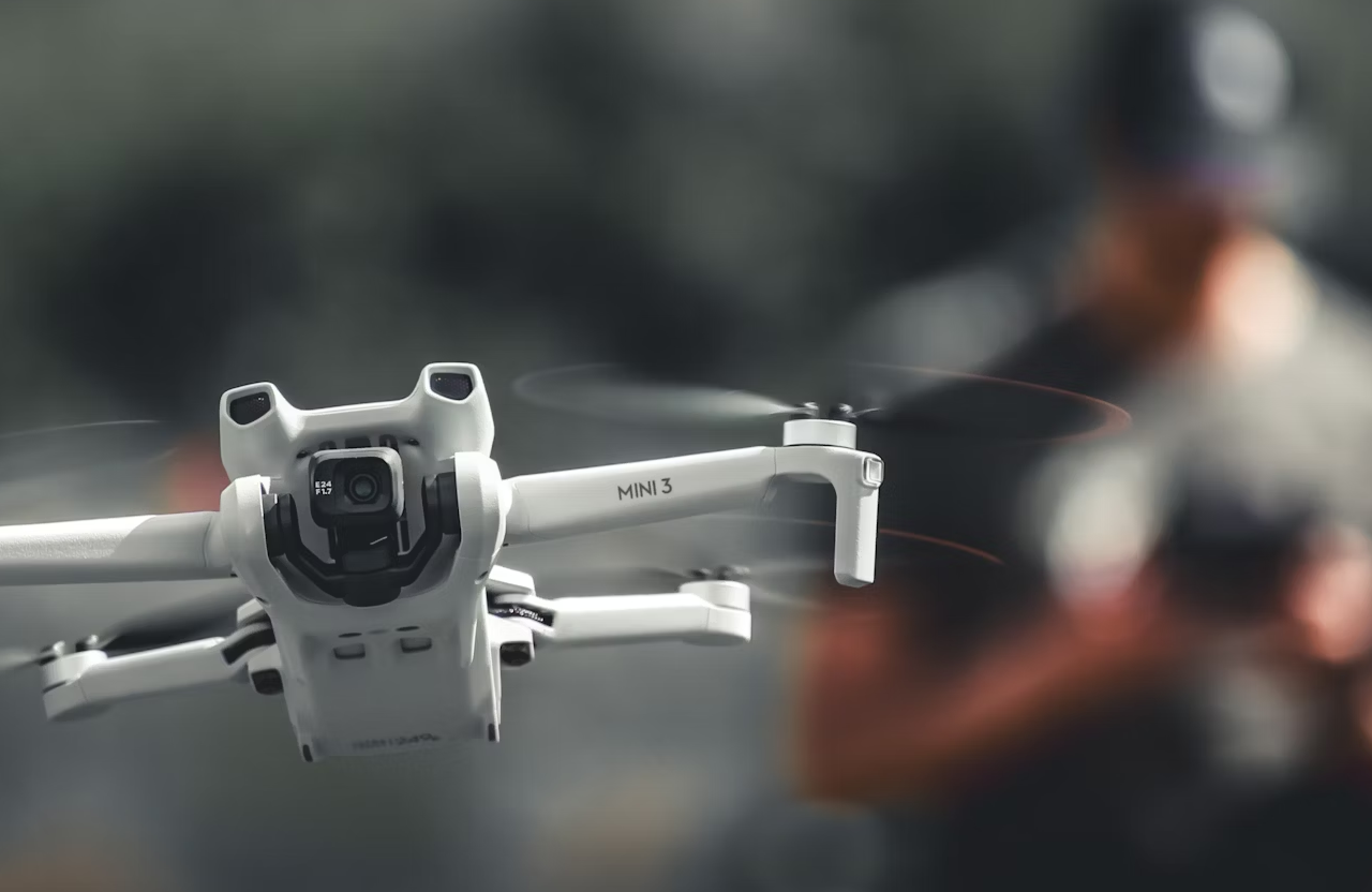 FX Productions Canada A white DJI Mini 3 drone hovers in the air with its camera facing forward; a person blurred in the background demonstrates professional drone services Toronto for precise aerial footage. Toronto Video Production Company