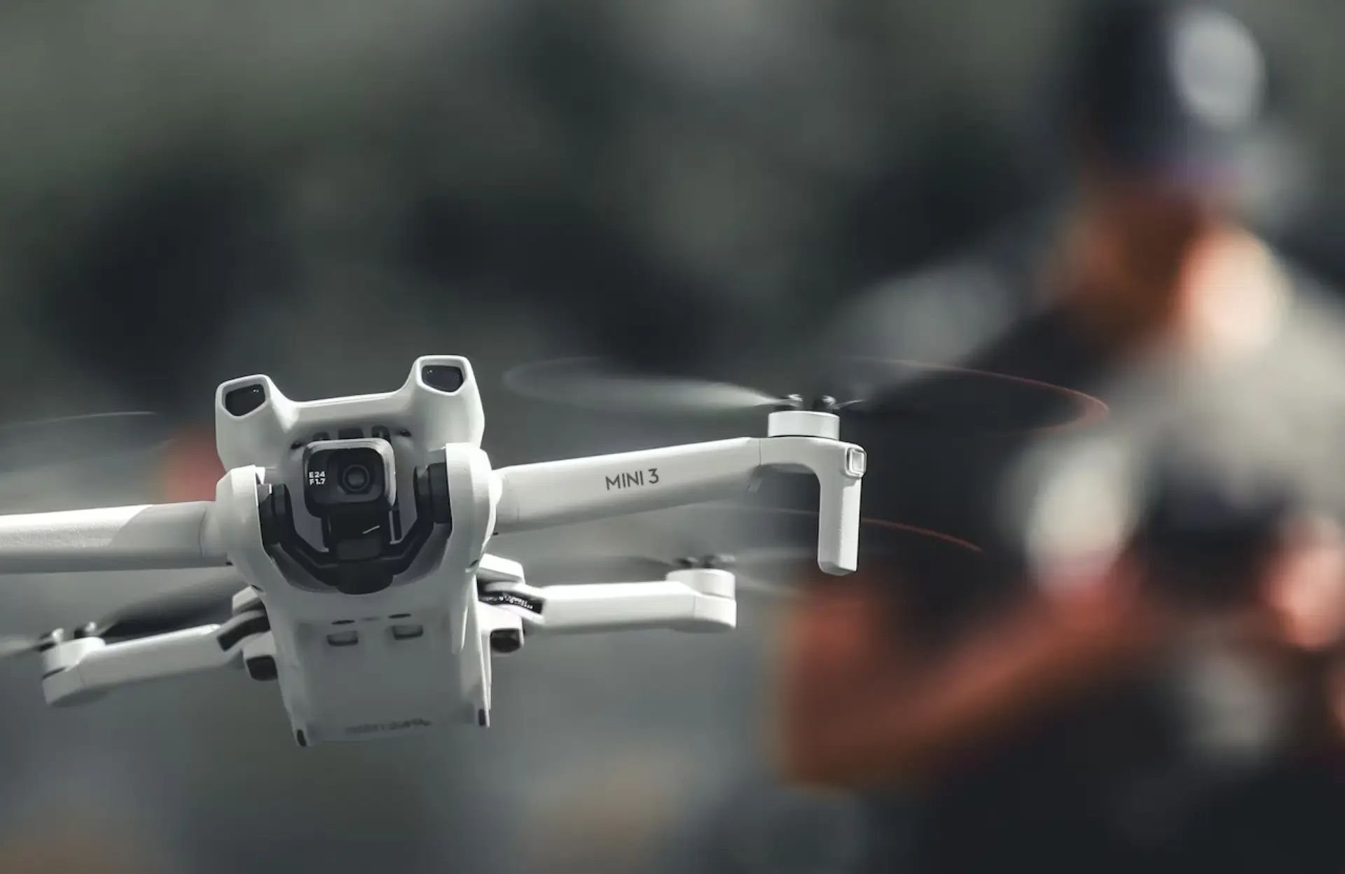 FX Productions Canada A white DJI Mini 3 drone hovers in the air with its camera facing forward; a person blurred in the background demonstrates professional drone services Toronto for precise aerial footage. Toronto Video Production Company