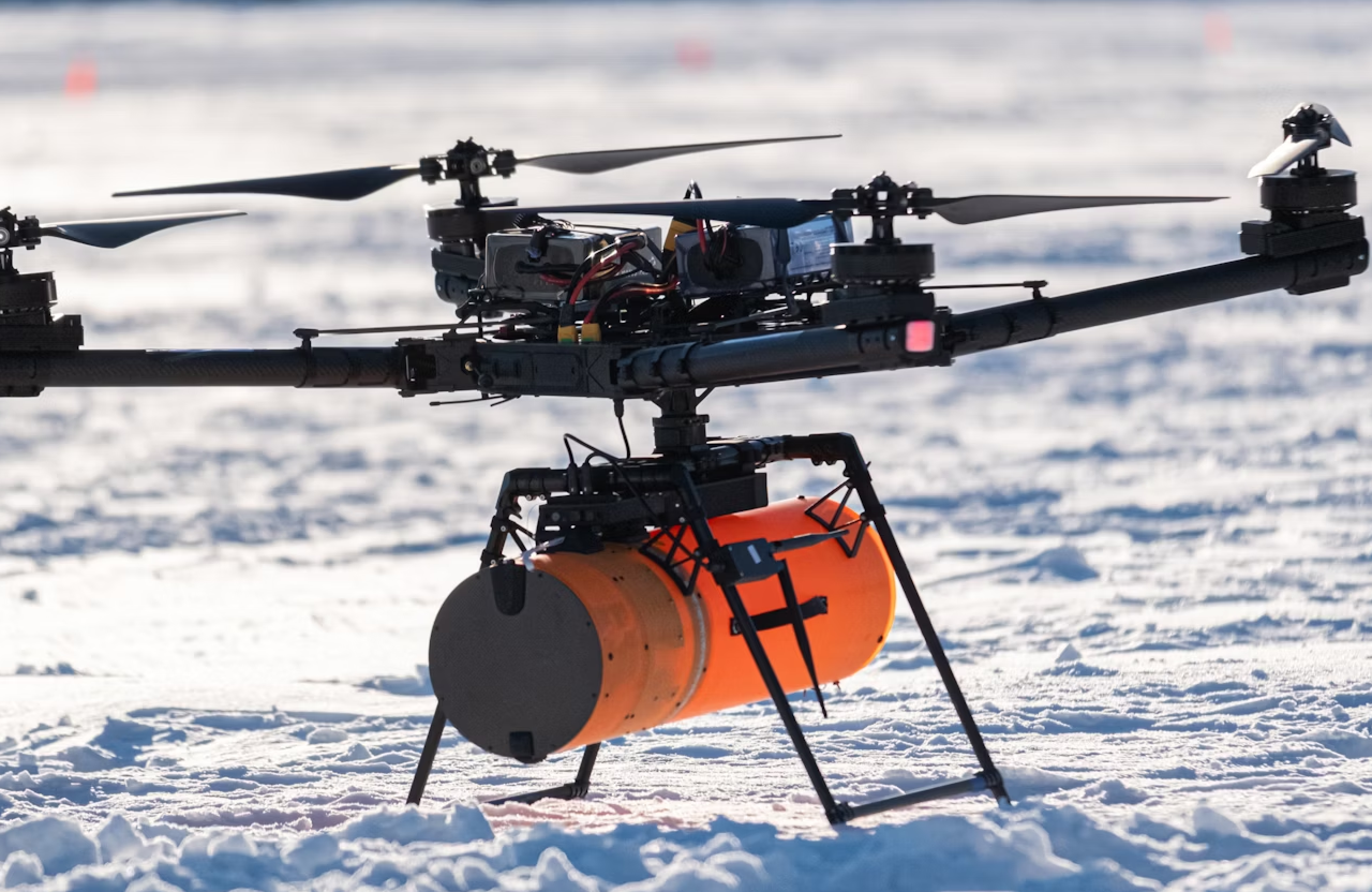 FX Productions Canada A large drone with six rotors stands on snow, carrying an orange cylindrical payload underneath—perfect for aerial cinematography and ideal for operators with RPAS certification. Toronto Video Production Company