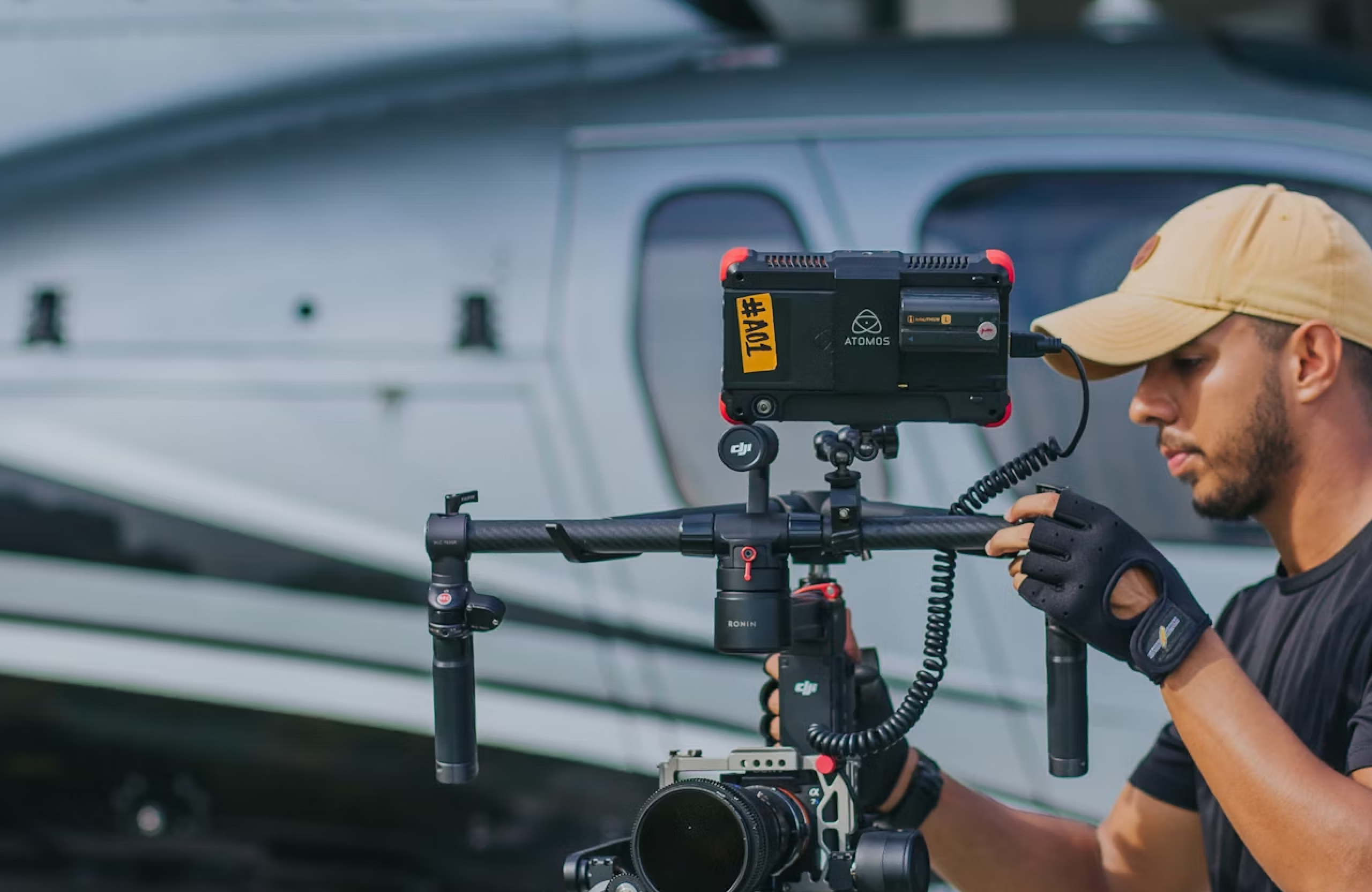 FX Productions Canada A person wearing a beige cap and gloves operates a professional camera rig with an attached monitor, showcasing expert aerial cinematography skills in front of a gray aircraft—ideal for those seeking RPAS certification. Toronto Video Production Company