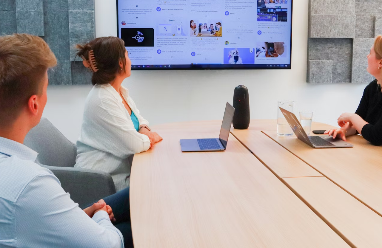 FX Productions Canada Three people seated at a conference table look at a large screen displaying a digital dashboard, with laptops and a speaker on the table. Toronto Video Production Company