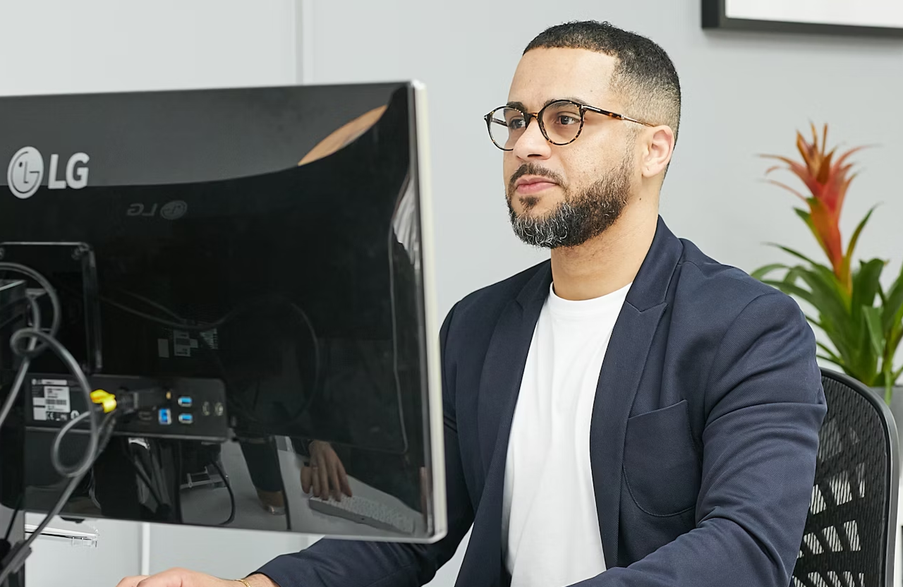 FX Productions Canada A man wearing glasses and a blazer sits at a desk, working on a desktop computer in an office setting. Toronto Video Production Company