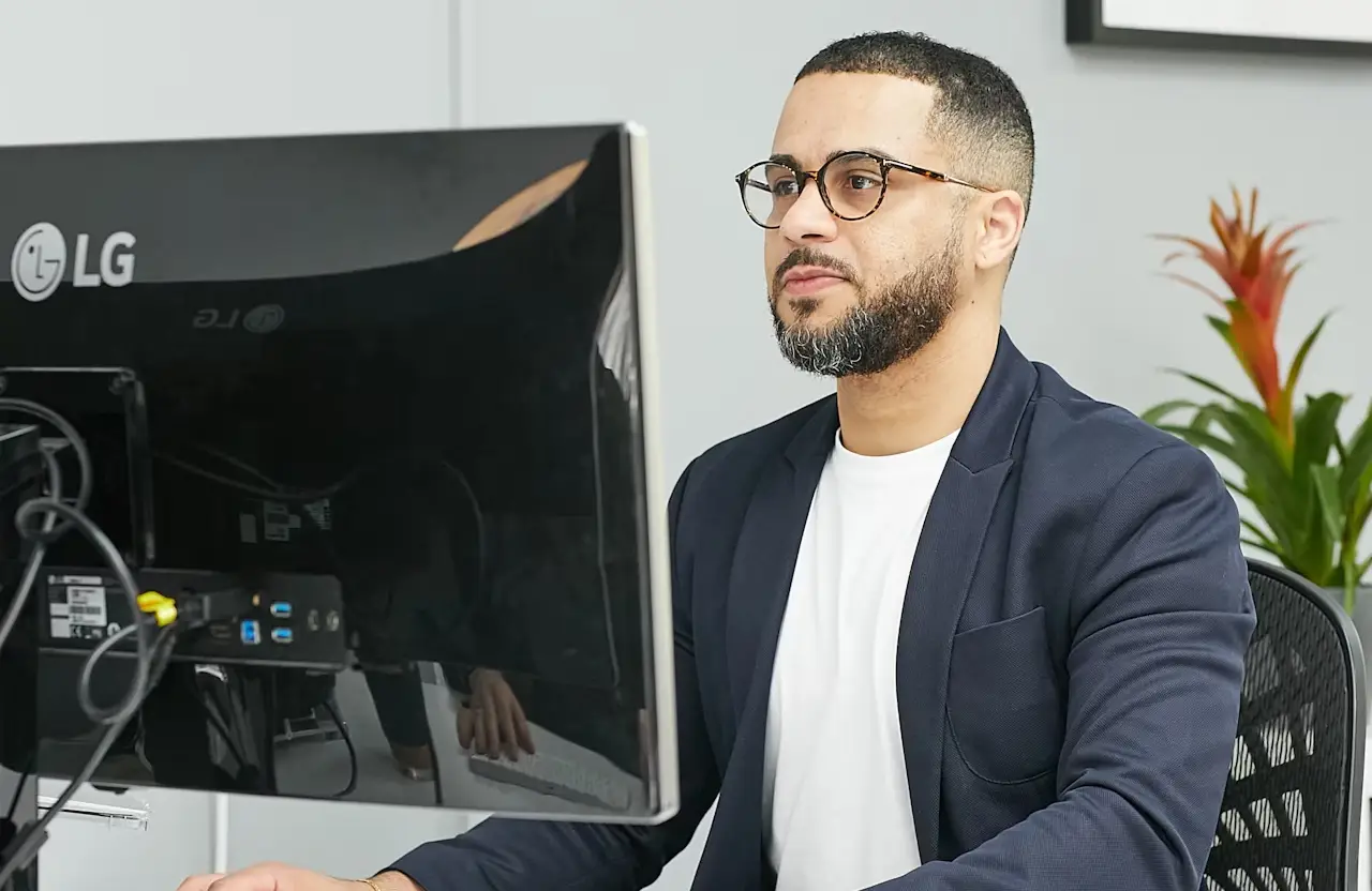FX Productions Canada A man wearing glasses and a blazer sits at a desk, working on a desktop computer in an office setting. Toronto Video Production Company