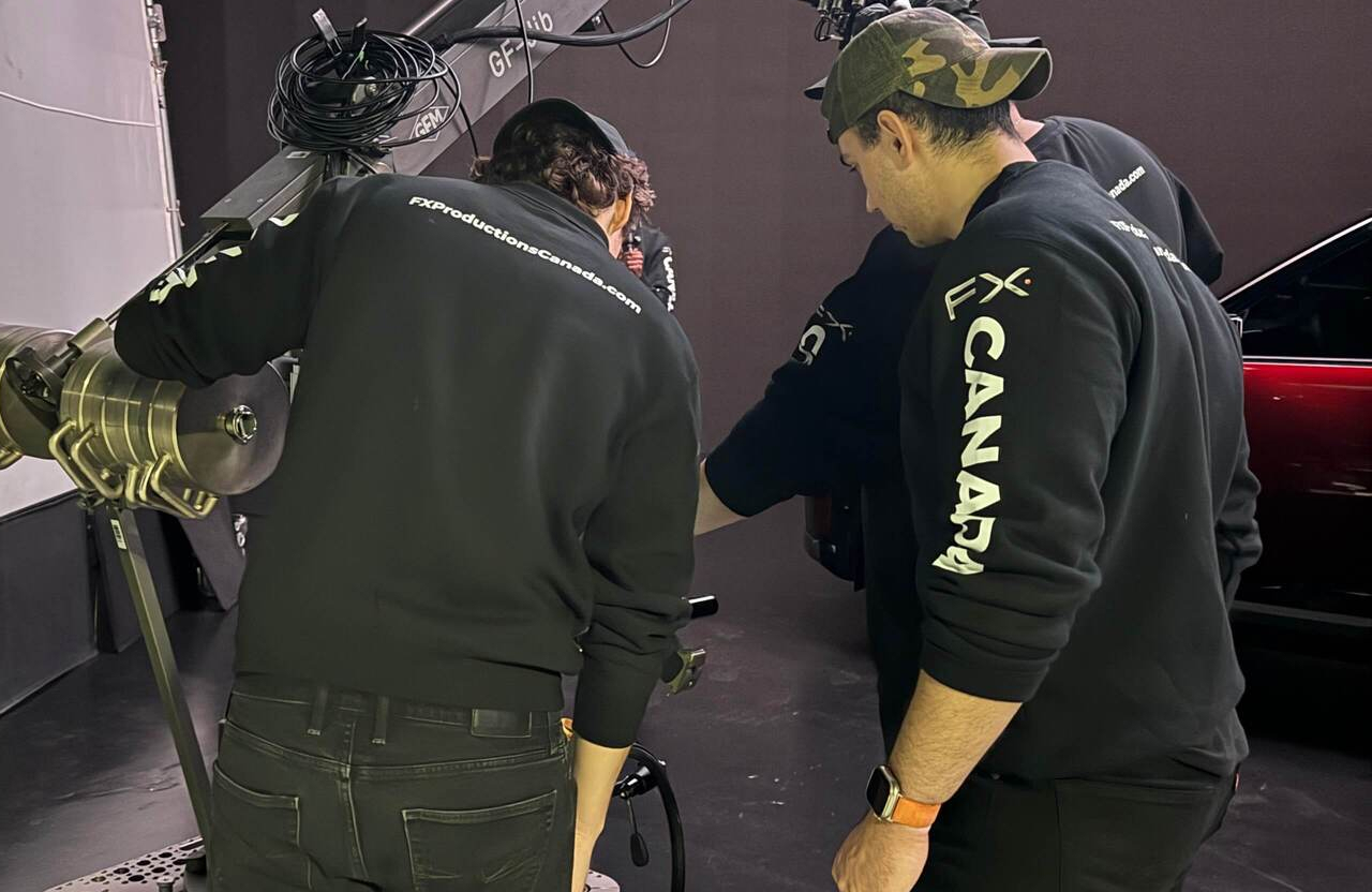 FX Productions Canada Three people wearing black FX CANADA sweatshirts work with film equipment next to a red car inside a studio. Toronto Video Production Company