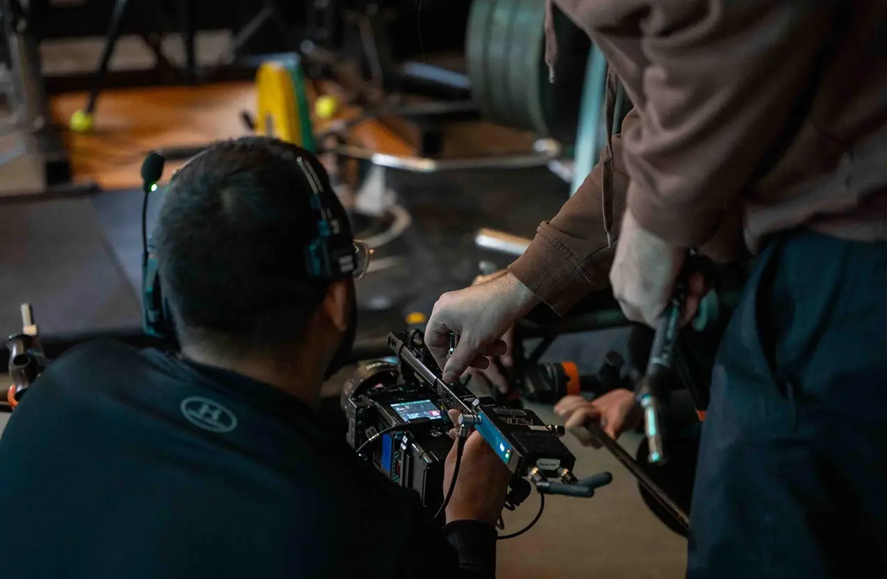 FX Productions Canada Two people wearing headsets adjust settings on a professional video camera in a dimly lit gym, embodying full service video production expectations with attention to detail and technical expertise. Toronto Video Production Company
