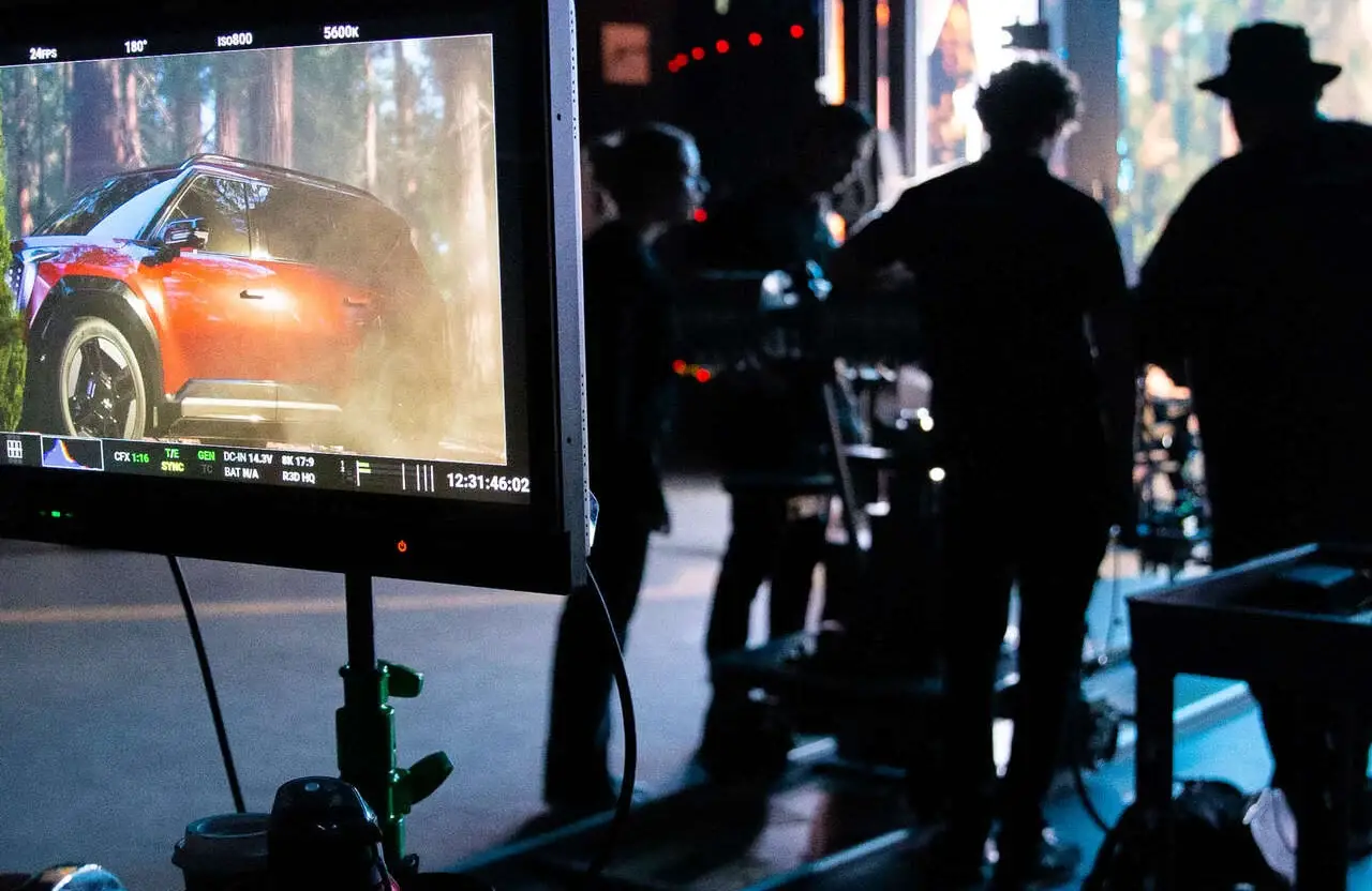 FX Productions Canada A camera monitor displays footage of a red SUV in a forest as crew members from a full service creative video production team work in silhouette on the film set behind. Toronto Video Production Company