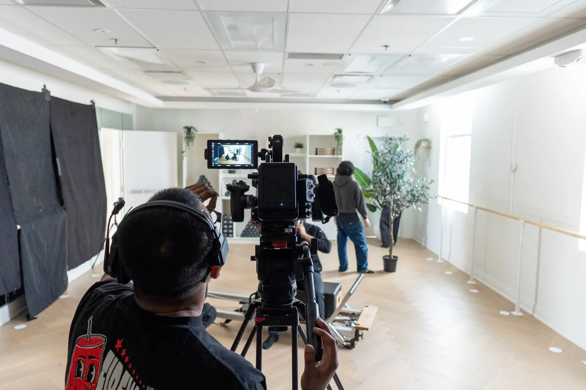 FX Productions Canada A person operates a camera on a tripod, filming another individual who is adjusting a potted plant in a well-lit indoor studio. Toronto Video Production Company