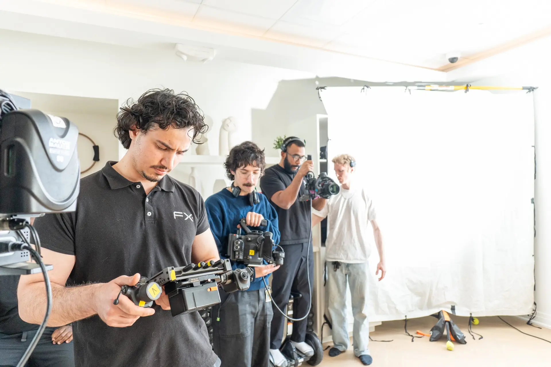 FX Productions Canada Four crew members operate cameras and equipment on a brightly lit film set, with a large white backdrop and various technical gear visible. Toronto Video Production Company
