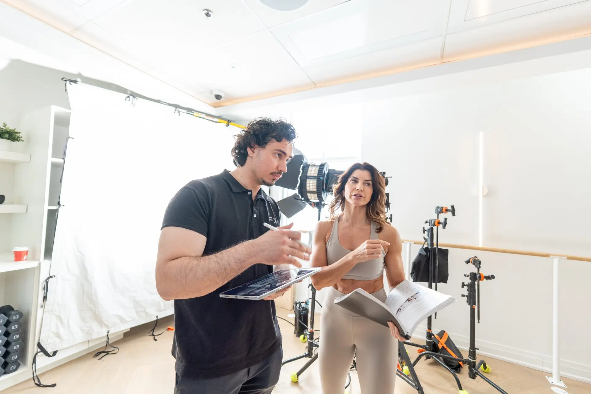 FX Productions Canada A man holding a laptop and a woman holding papers have a discussion in a brightly lit studio with lighting equipment in the background. Toronto Video Production Company