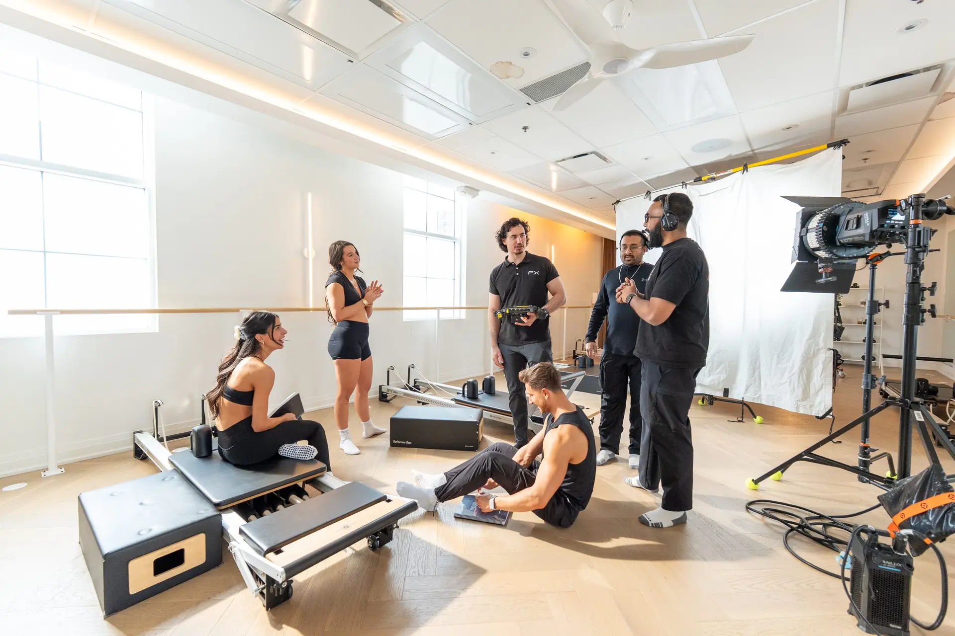 FX Productions Canada A group of people in athletic wear interact with a film crew in a brightly lit fitness studio with equipment and cameras visible. Toronto Video Production Company