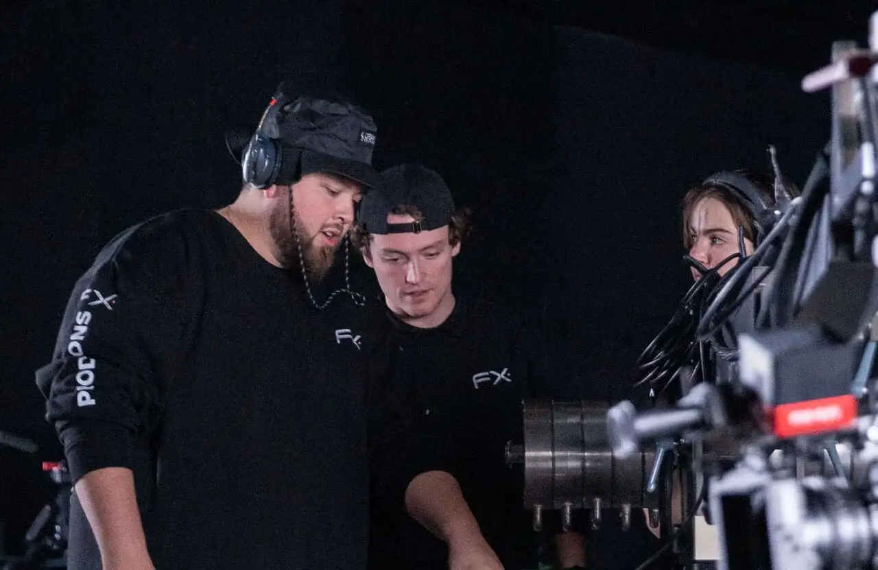 FX Productions Canada Three people wearing headsets and black FX shirts collaborate in a dimly lit studio, focusing on equipment as they ensure compliance during a corporate video production. Toronto Video Production Company