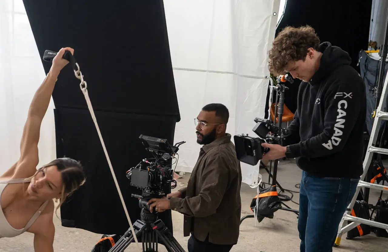 FX Productions Canada A woman exercises with resistance bands while two men film her using professional camera equipment in a studio setting. Toronto Video Production Company