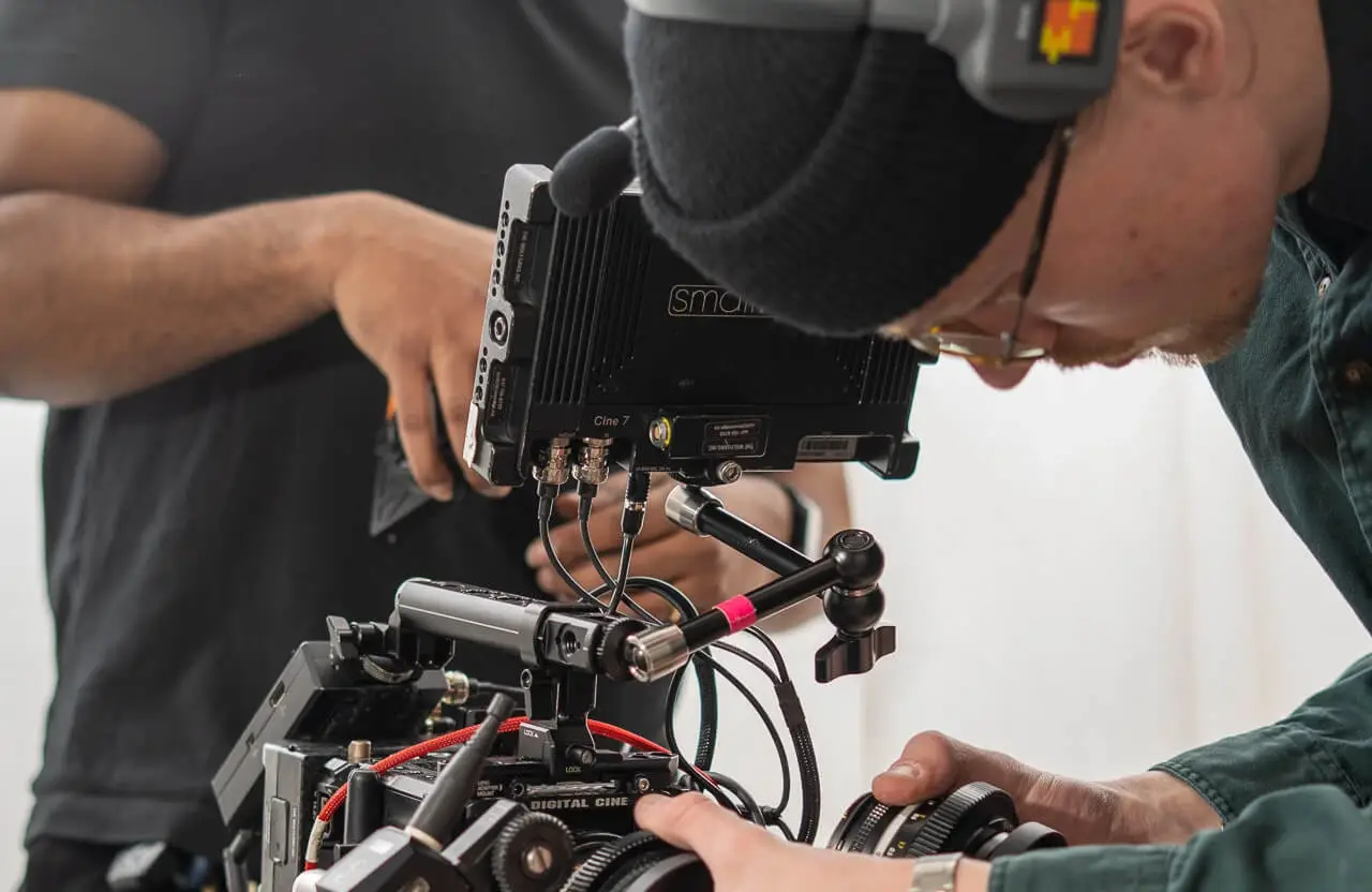 FX Productions Canada Two people adjust a professional video camera setup; one wears headphones and a beanie while focusing closely on the equipment. Toronto Video Production Company