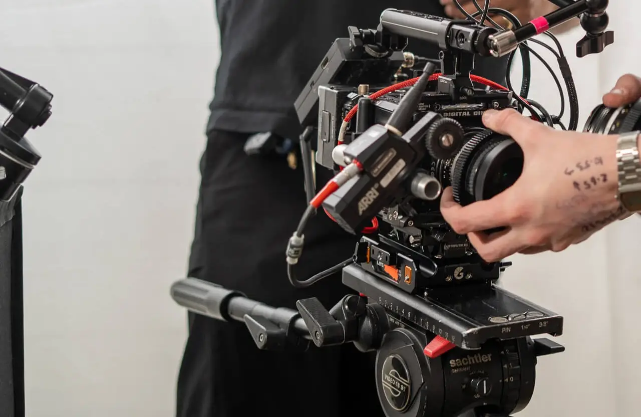 FX Productions Canada A person adjusts the lens on a professional video camera mounted on a tripod, with cables and equipment visible. Toronto Video Production Company