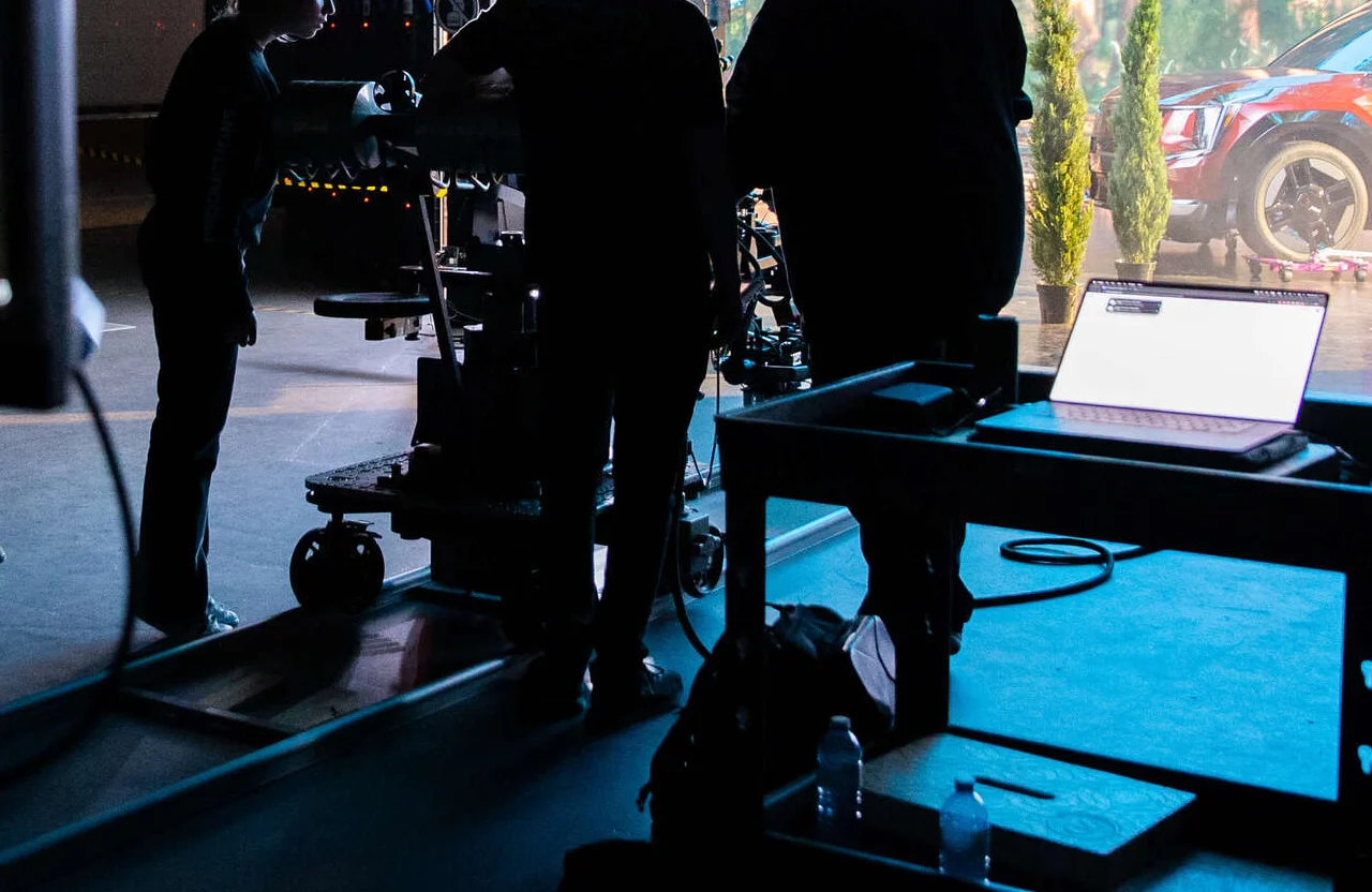 FX Productions Canada Several people are silhouetted against a brightly lit set in Canada's Video Production Capital, with camera equipment, a laptop on a cart, and a parked car visible through a glass wall. Toronto Video Production Company