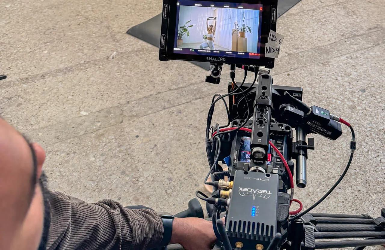 FX Productions Canada Person operates a professional camera rig on set, illustrating how production quality affects brand perception; a monitor displays a woman standing in a room with plants and curtains in the background. Toronto Video Production Company