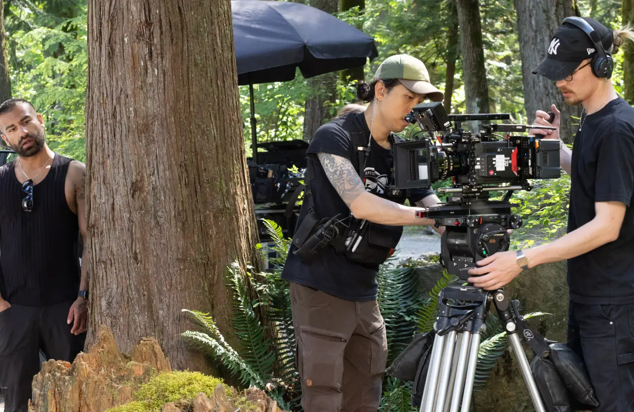 FX Productions Canada Three people work outdoors with professional film equipment; one operates a camera on a tripod, another adjusts controls, and a third person stands by a tree observing the scene, perhaps getting ready to compare video production quotes for their next project. Toronto Video Production Company