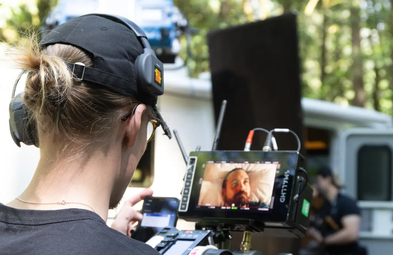 FX Productions Canada A person wearing a headset operates a camera with a monitor displaying a close-up of a man lying down, outdoors in daylight, capturing footage as part of a video production contract. Toronto Video Production Company
