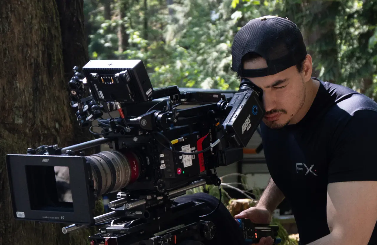 FX Productions Canada A man in a black shirt and cap operates a large professional video camera outdoors, surrounded by trees and greenery—a scene that highlights the importance of spotting red flags when hiring a video production company. Toronto Video Production Company