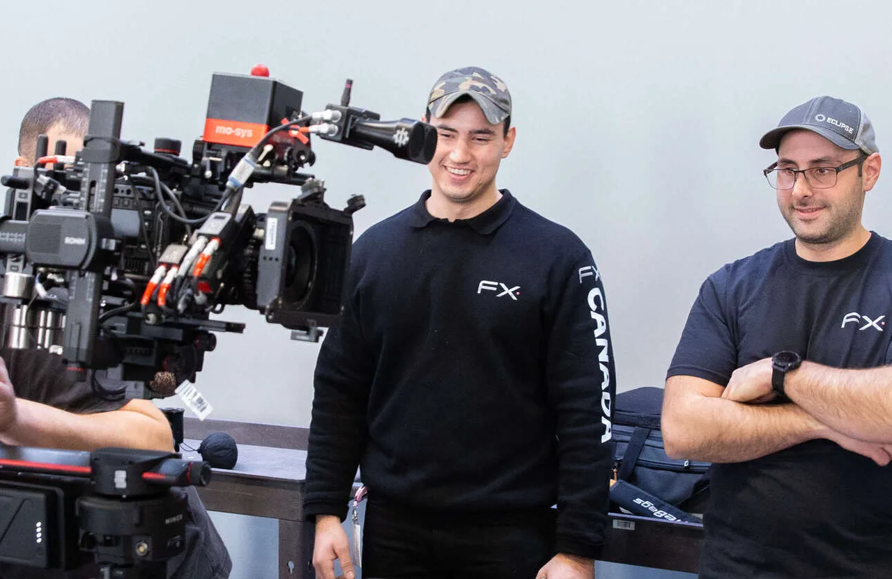 FX Productions Canada Two men wearing FX Canada shirts stand in front of a professional video camera setup, with equipment visible in the background, exemplifying their commitment to delivering projects with Long-Term Business Impact. Toronto Video Production Company