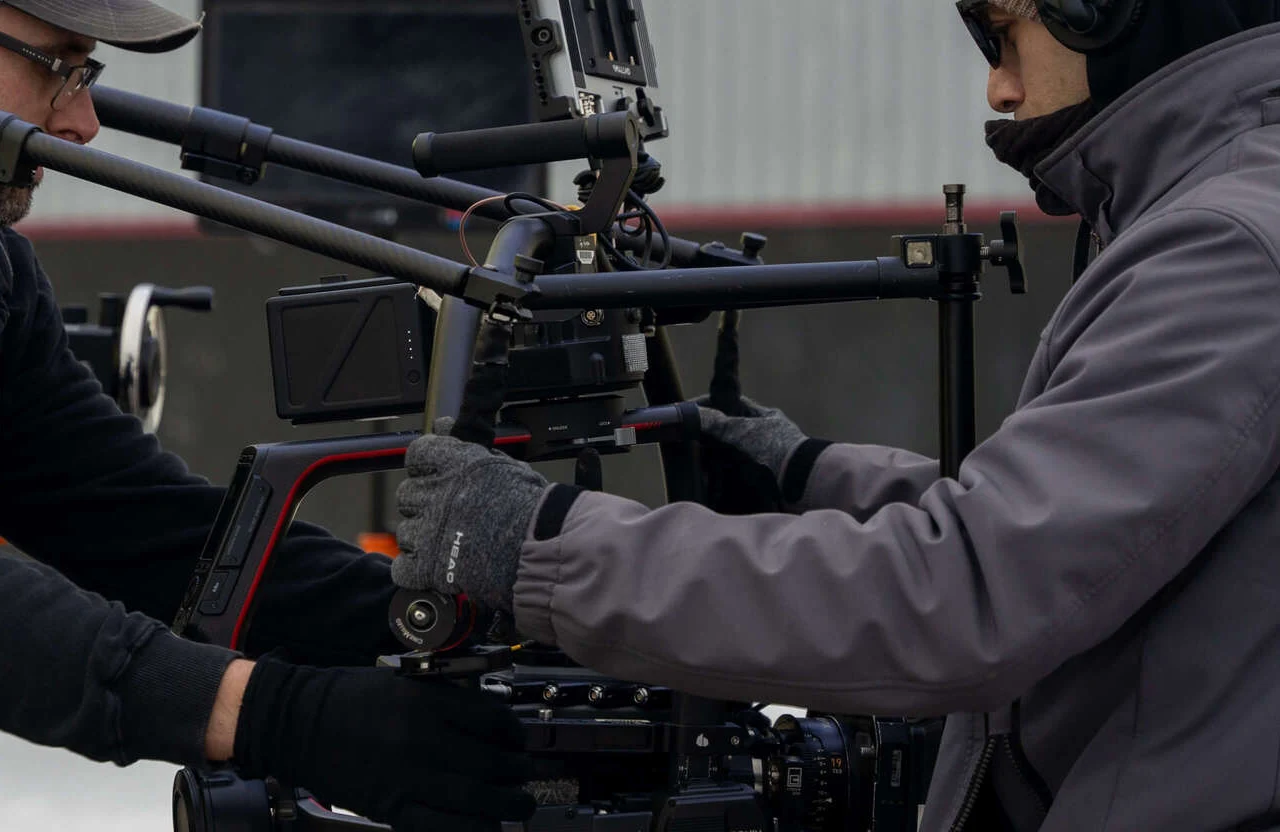 FX Productions Canada Two people wearing gloves and jackets adjust a professional video camera rig outdoors, showcasing the teamwork and expertise behind cheap video production Toronto services. Toronto Video Production Company