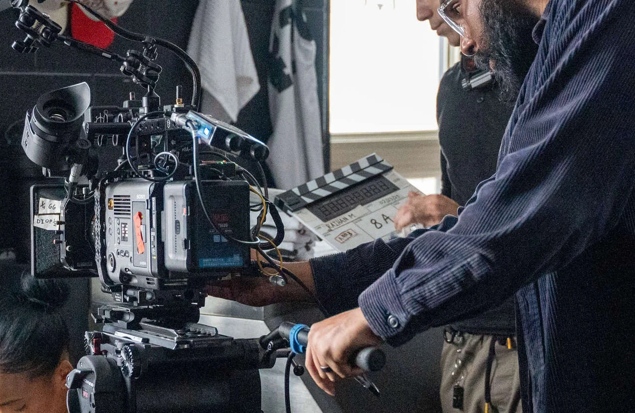 FX Productions Canada Two crew members, part of a skilled video production partner Toronto team, operate a professional video camera and prepare a film slate on a set with equipment visible in the background. Toronto Video Production Company