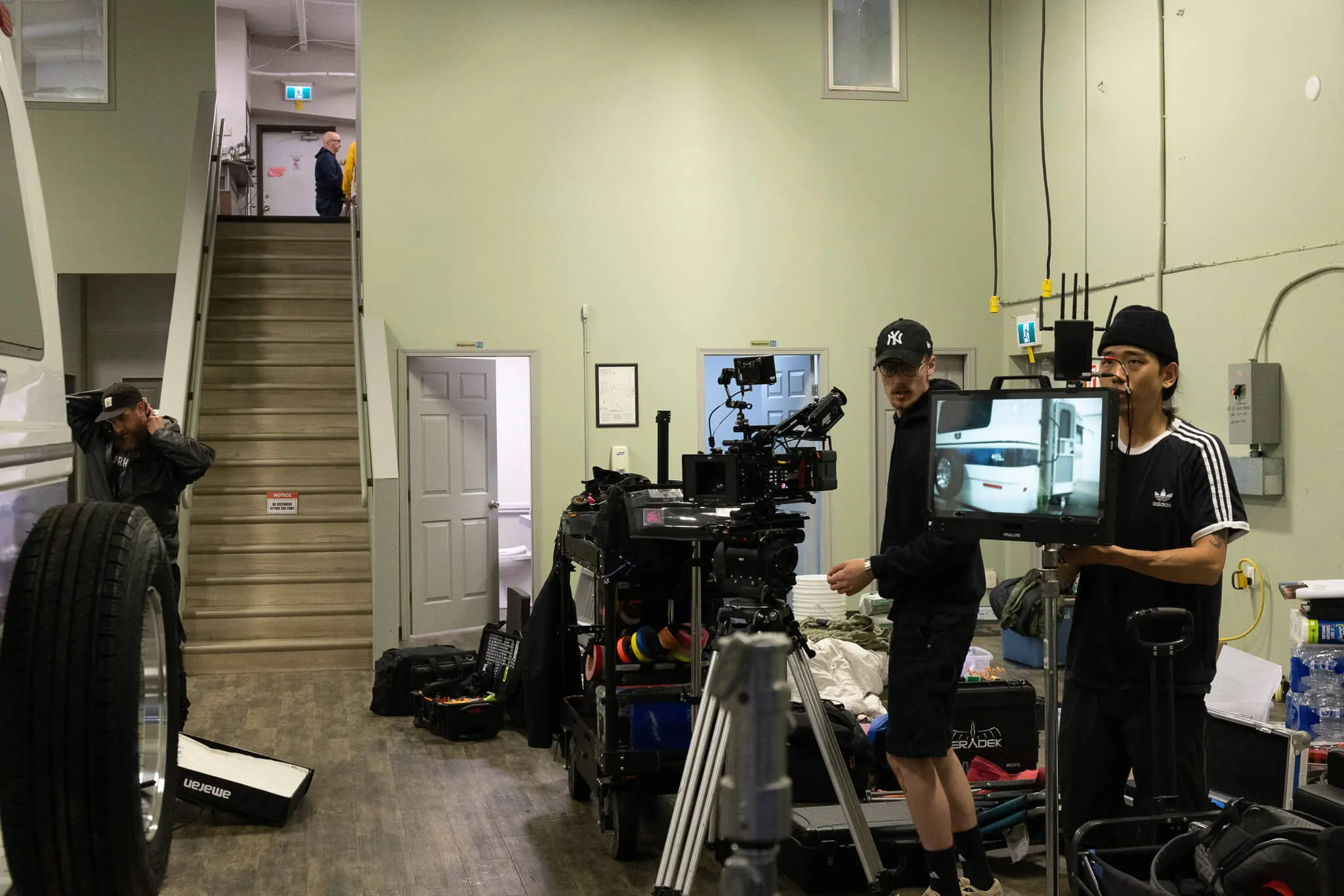 FX Productions Canada Two crew members operate a camera setup in a room filled with film equipment, showcasing firsthand why video production is important; another person stands near a staircase in the background. Toronto Video Production Company