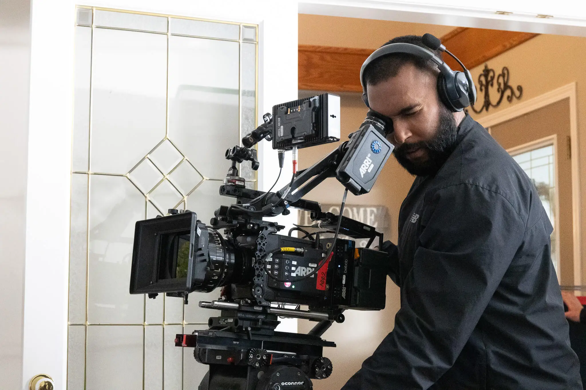 FX Productions Canada A person wearing headphones operates a professional ARRI video camera indoors near a glass door, capturing footage for a project overseen by a skilled video editor in Vancouver. Toronto Video Production Company