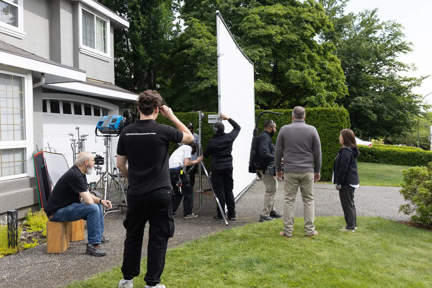 FX Productions Canada A film crew sets up lighting and equipment outside a house, with several people adjusting gear and others observing on a driveway and lawn—typical of video production for outdoor brands in Vancouver. Toronto Video Production Company