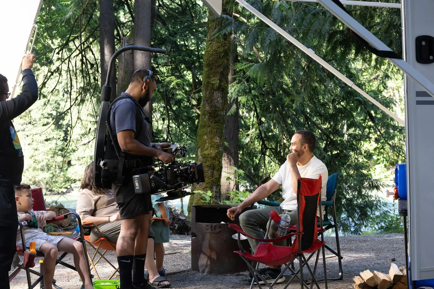 FX Productions Canada A film crew records a man sitting in a red camping chair at a campsite, surrounded by trees and other people, with camera equipment visible—a scene that highlights why Vancouver is such a popular filming location, thanks to its scenic natural landscapes and versatile backdrops. Toronto Video Production Company