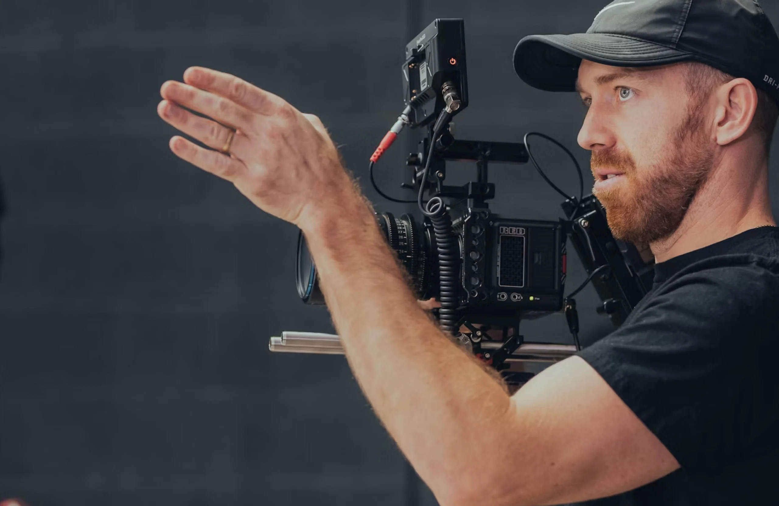 FX Productions Canada Man wearing a cap operates a professional video camera, gesturing with his hand while looking intently ahead—a focused videographer in Vancouver capturing the perfect shot. Toronto Video Production Company