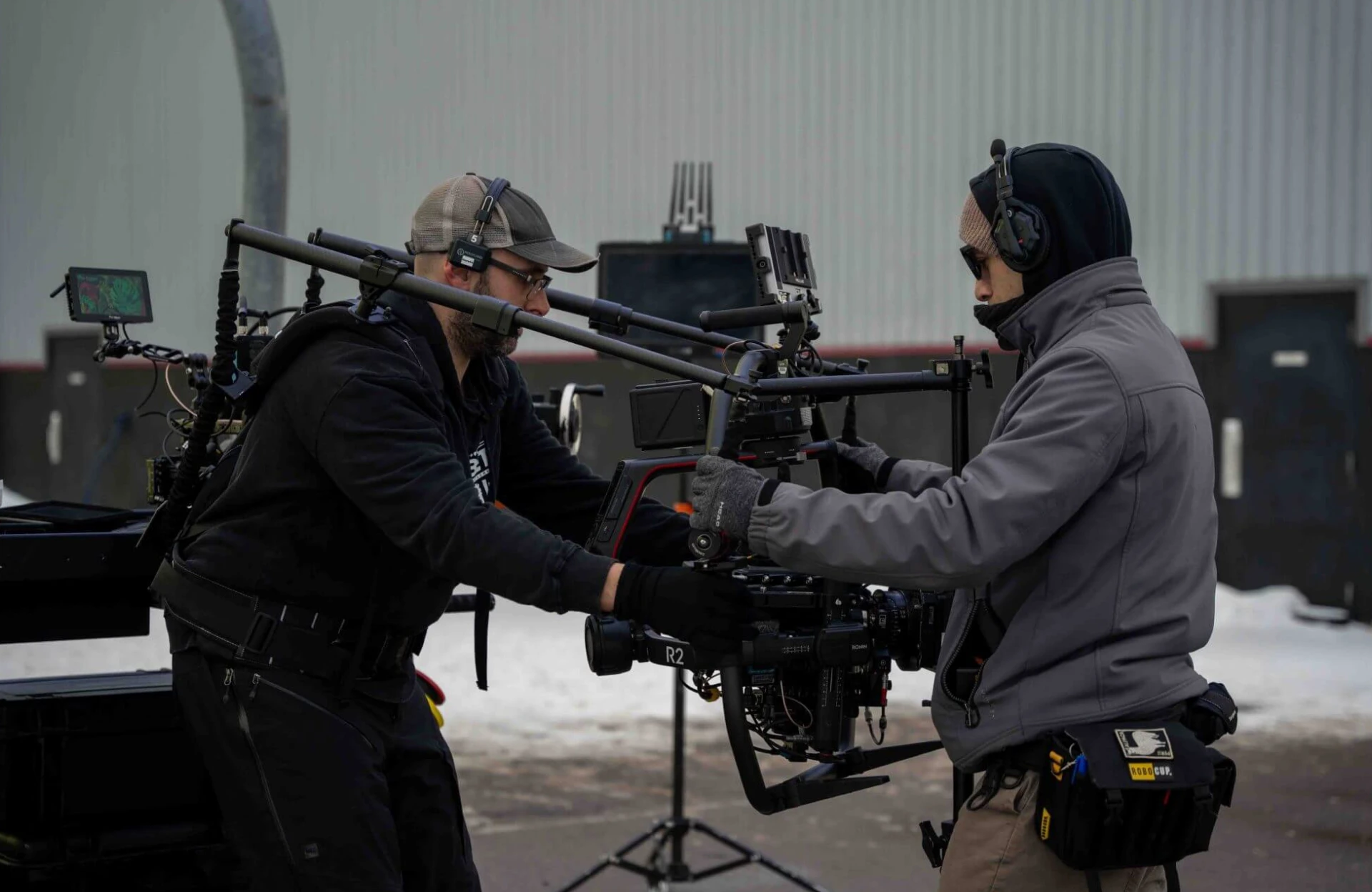 FX Productions Canada Two crew members wearing headsets adjust a professional camera rig outdoors near industrial buildings on a snowy day, capturing footage that will later benefit from expert post-production—especially when considering the hourly rate for video editing services. Toronto Video Production Company