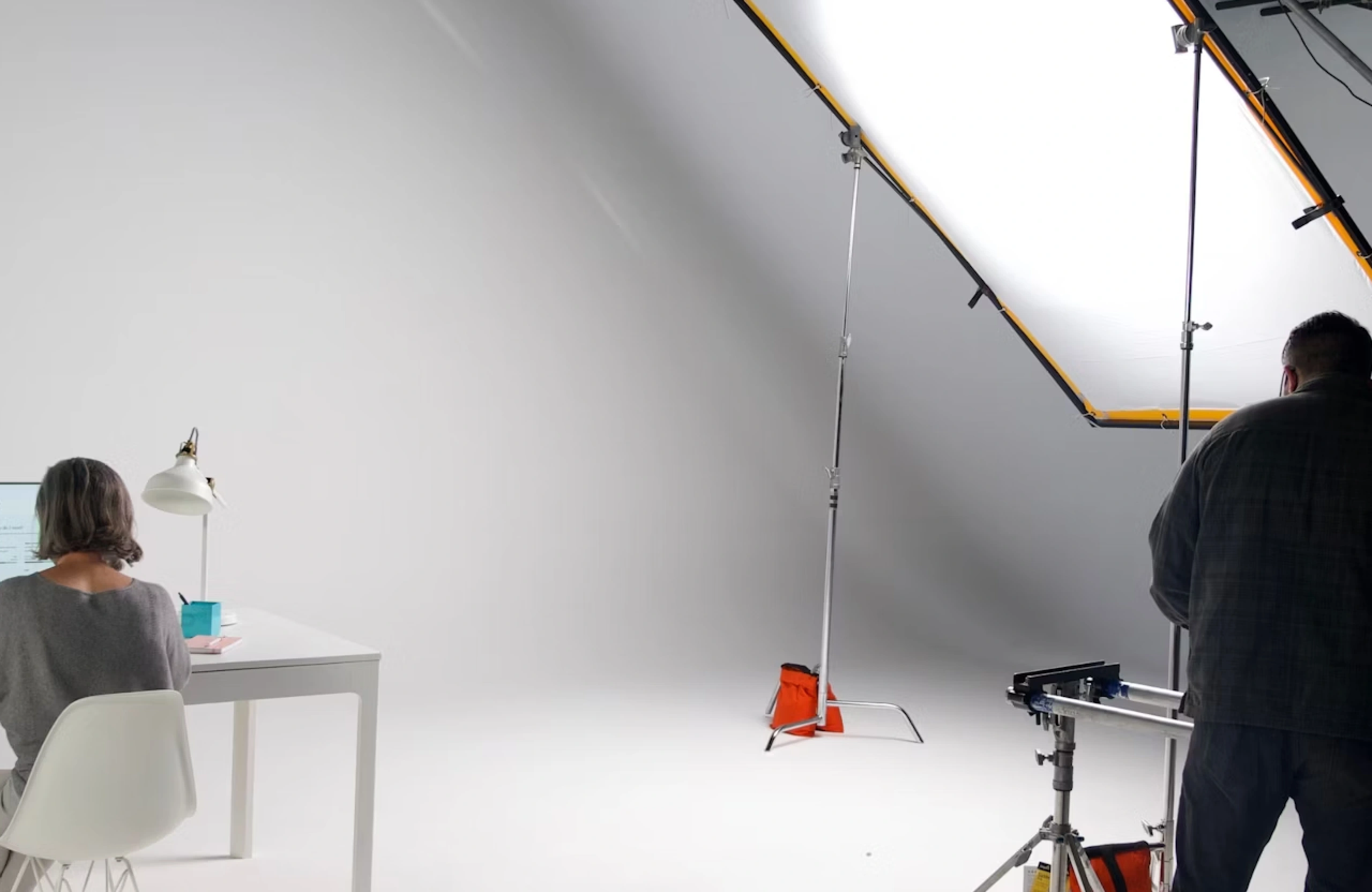 FX Productions Canada A woman works at a white desk while a photographer stands near lighting equipment in a professional studio with a white backdrop, capturing the dynamic energy of a Vancouver brand film production. Toronto Video Production Company