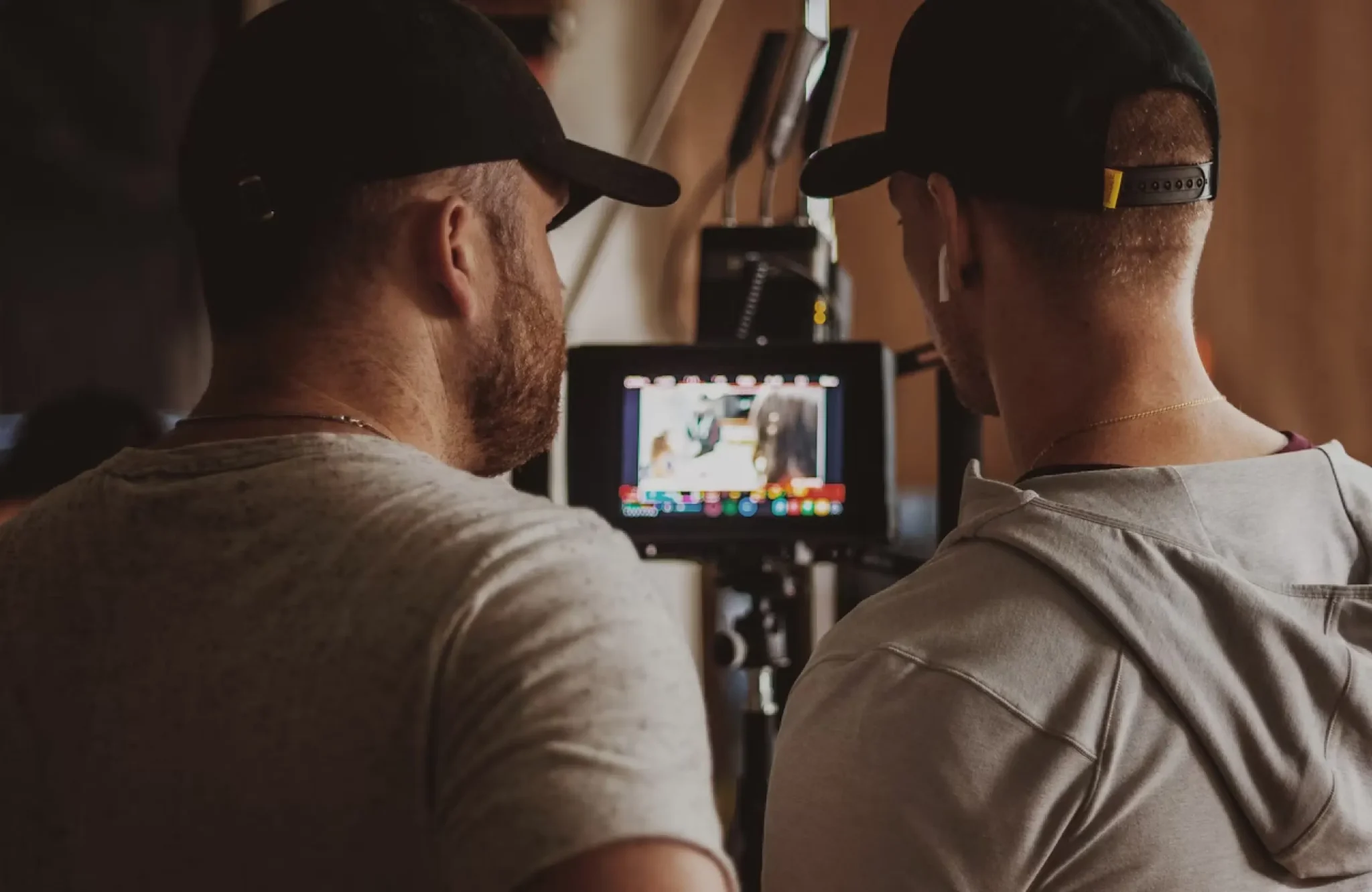 FX Productions Canada Two men wearing caps view footage on a monitor, likely on a film or video set, with their backs facing the camera—an ideal moment that highlights why it’s important to consider questions to ask a videographer before hiring, ensuring you capture exactly the scenes you envision. Toronto Video Production Company